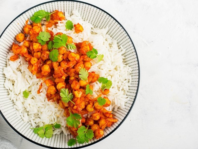 Ein Teller Kichererbsen-Erdnuss-Curry mit Reis und Koriander in der Draufsicht.