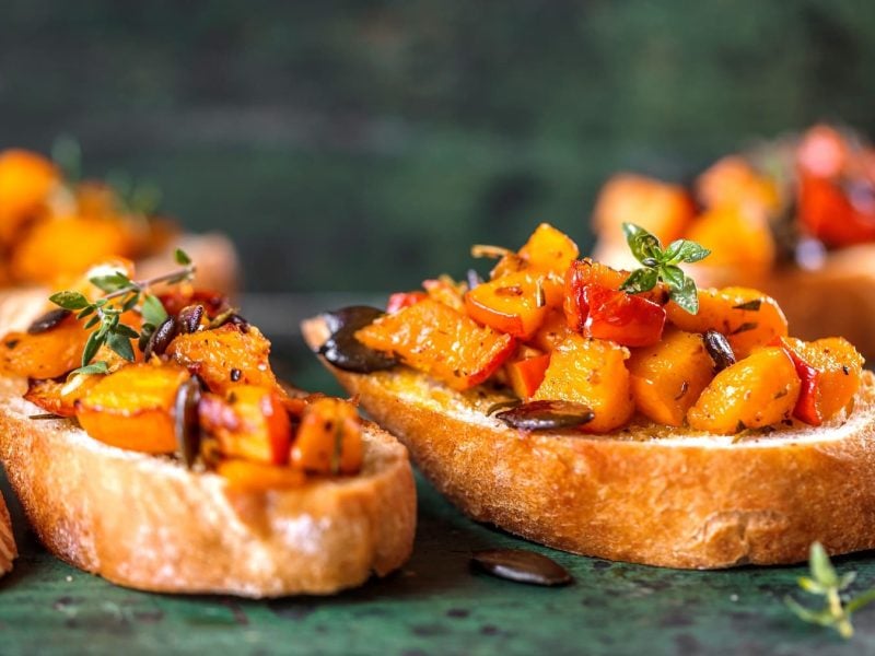 Mehrere Kürbis-Bruschetta mit Kürbiskernen und frischen Kräutern.