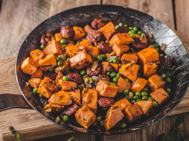 Kürbis-Erbsen-Pfanne mit veganer Chorizo auf einem Holzbrett.