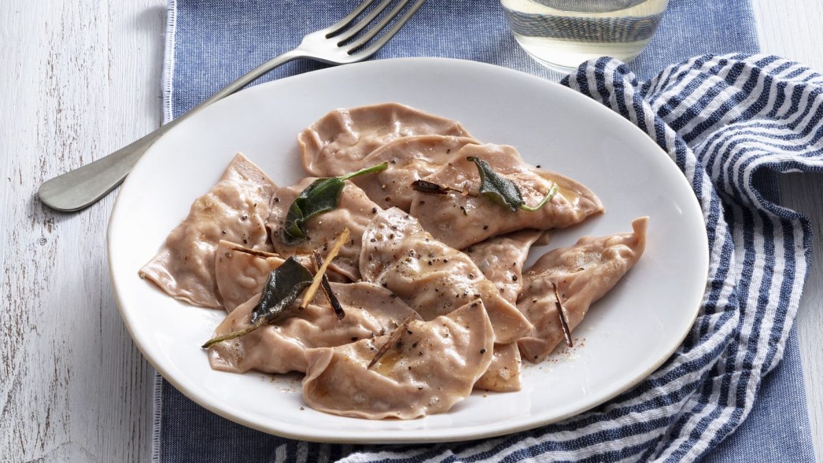 Ein weißer Teller mit Maronen-Ravioli auf einem blau gestreiften Tuch.