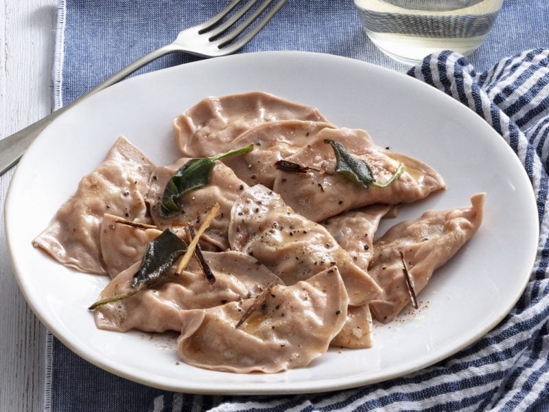 Ein weißer Teller mit Maronen-Ravioli auf einem blau gestreiften Tuch.