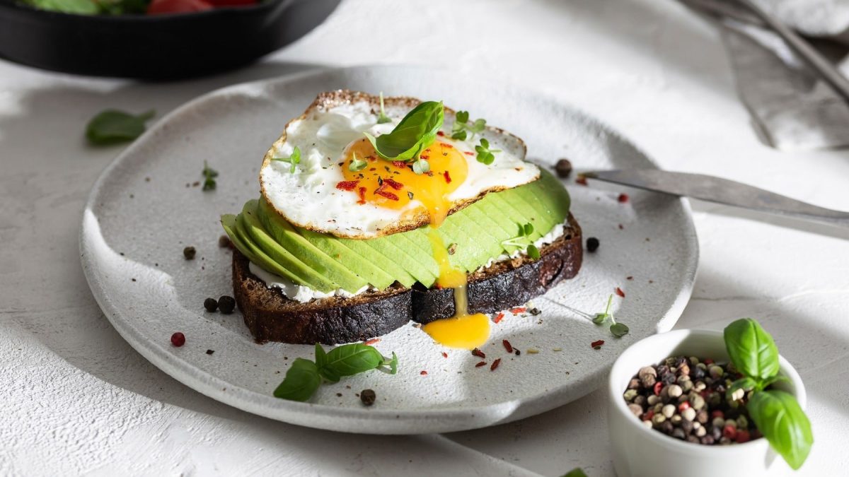 Pumpernickel-Frühstück mit Spiegelei und Avocado, serviert auf einem Teller mit Kresse und Baslikum garniert.