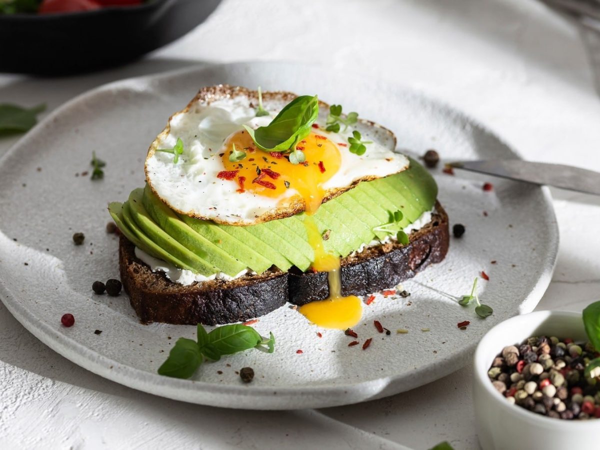 Pumpernickel-Frühstück mit Spiegelei und Avocado, serviert auf einem Teller mit Kresse und Baslikum garniert.