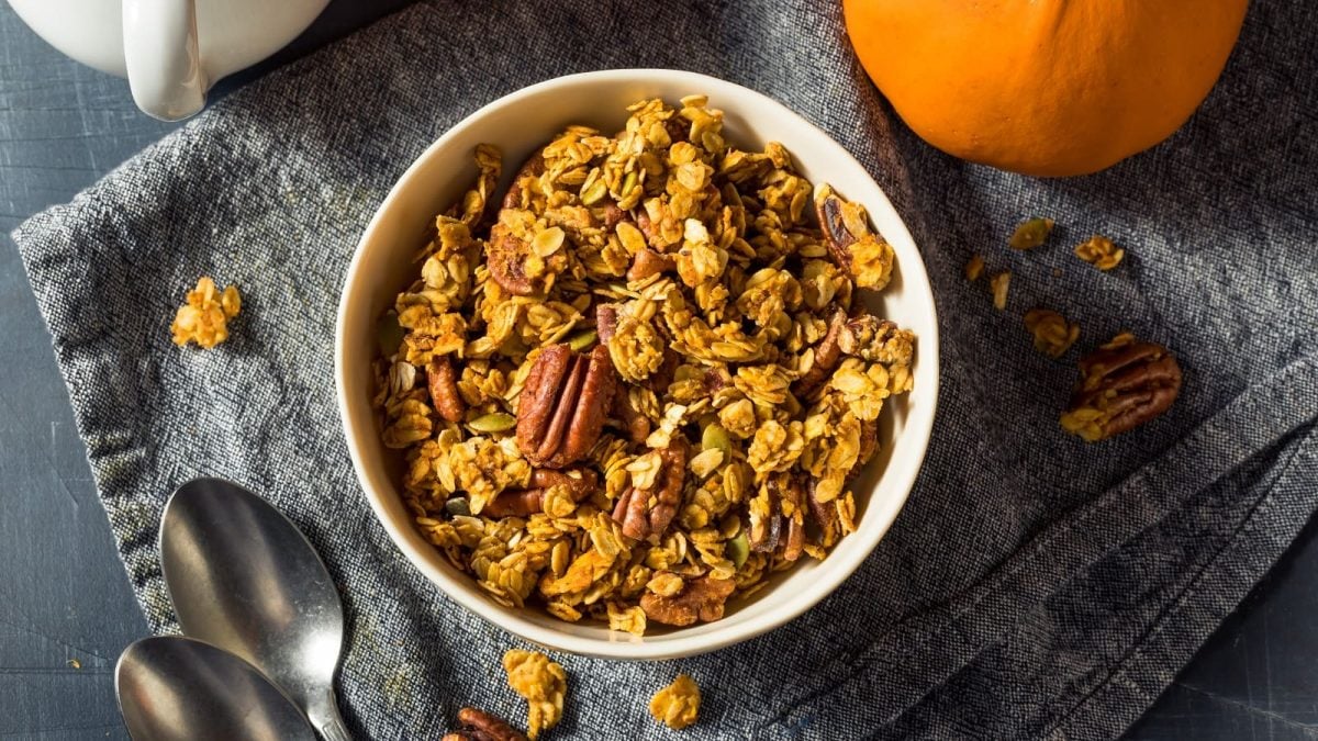 Eine weiße Schüssel auf einem blauen Tuch mit Pumpkin Spice Granola darauf.