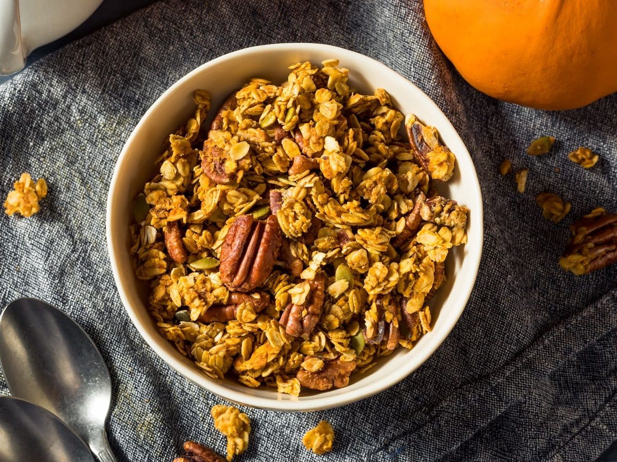 Eine weiße Schüssel auf einem blauen Tuch mit Pumpkin Spice Granola darauf.