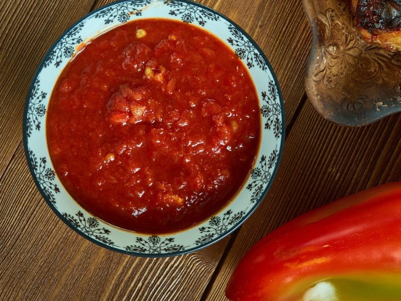 Salsa Ranchera in blau-weißer Schale auf Holztisch. Daneben Paprika und Toastbrot auf Teller. Draufsicht.