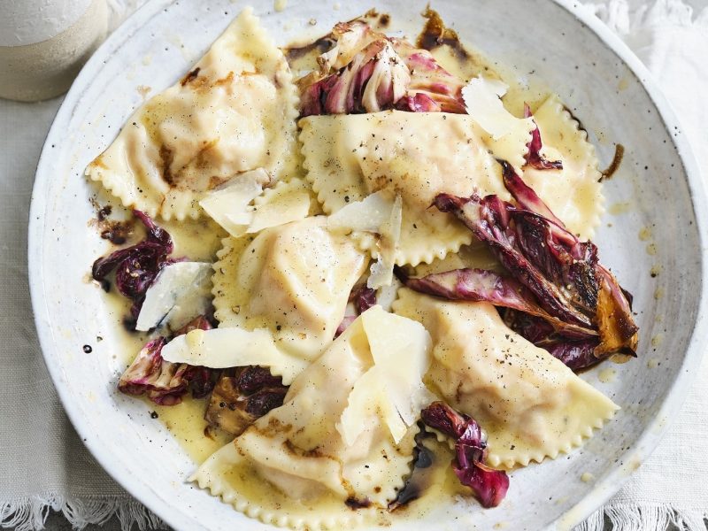 Schlutzkrapfen mit Kürbisfüllung und Radicchio auf einem weißen Teller vor weißem Hintergrund.