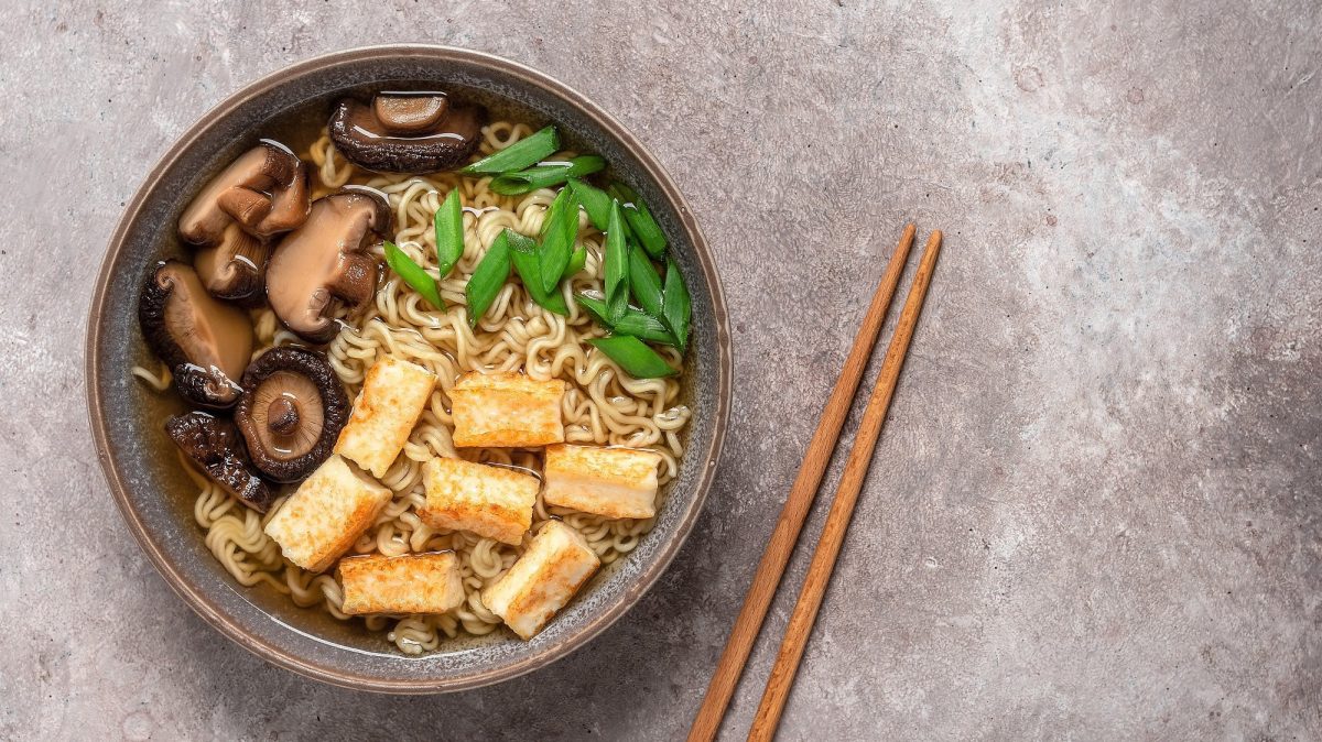 Eine Schüssel schnelle Ramen mit Pilzen, Tofu und Frühlingszwiebeln, daneben Essstäbchen, alles Draufsicht.