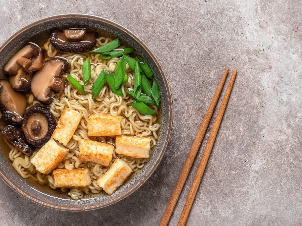 Eine Schüssel schnelle Ramen mit Pilzen, Tofu und Frühlingszwiebeln, daneben Essstäbchen, alles Draufsicht.