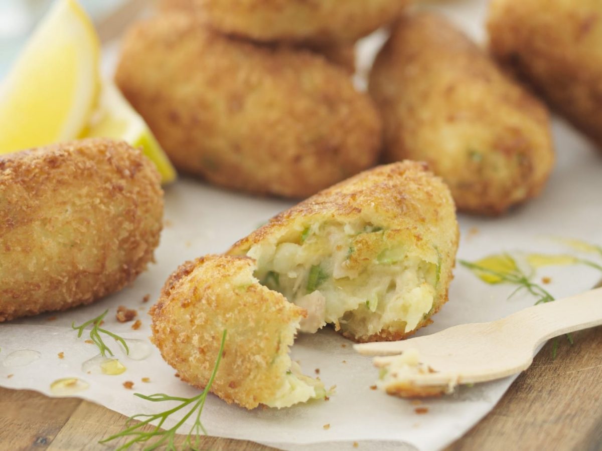 Selbst gemachte Thunfisch-Kroketten, angeschnitten serviert auf einem hellen Backpapier, garniert mit frischem Dill und serviert mit Zitronenstücken.