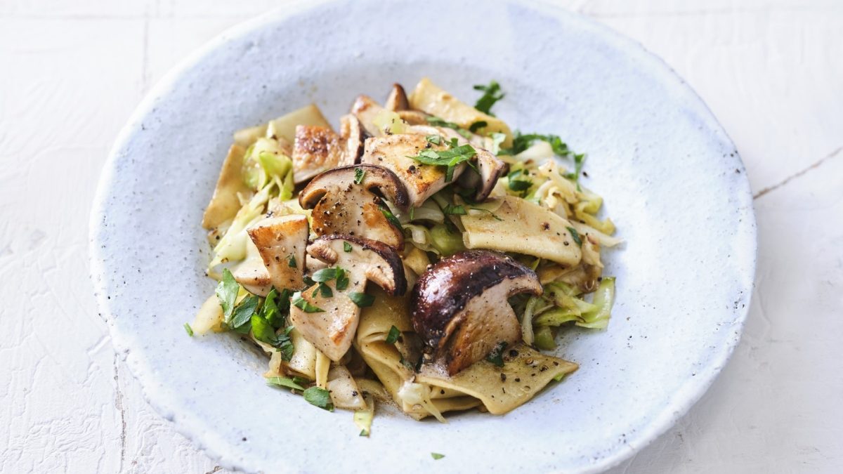 Selbst gemachte Fleckerl mit Steinpilzen und Spitzkohl, in einer weißen Schale serviert und mit frischer Petersilie garniert.