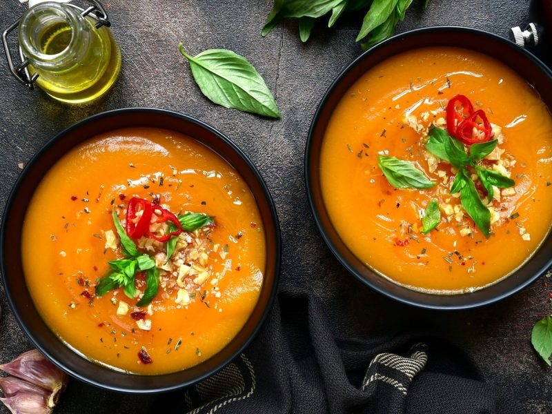 Zwei schwarze Schüsseln mit Spiced Hokkaido-Suppe neben frischen Zutaten auf einem dunklen Tisch.