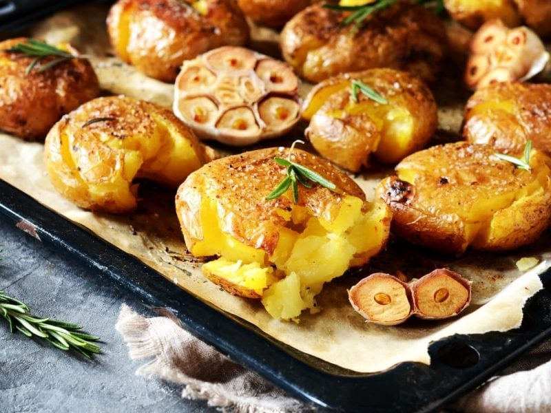 Smashed Garilc-Potatoes auf Backblech. Davor Rosmarinzweig. Draufsicht.