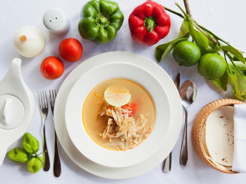 Sopa de Lima mexikanische Hühnersuppe auf Suppenteller auf Teller. Kreisförmig diverse Zutaten um den Teller herum angerichtet. Draufsicht.