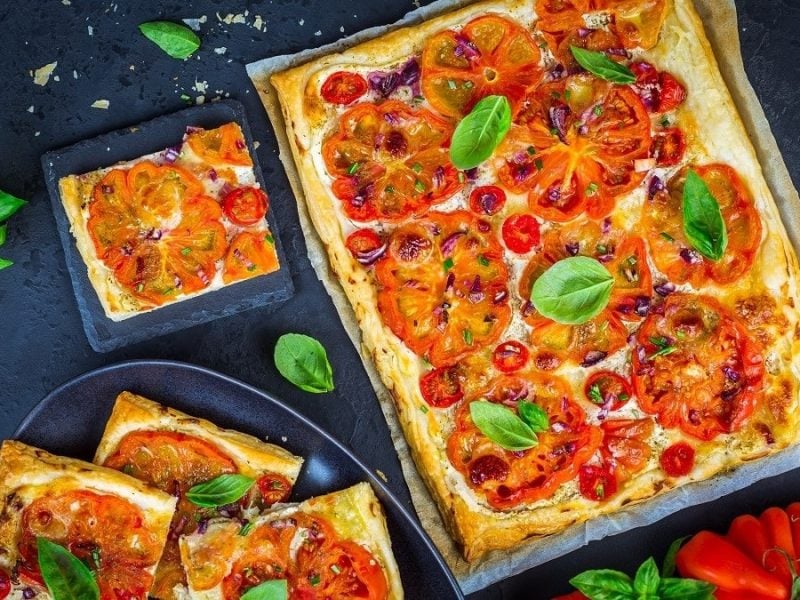 Vogelperspektive: Ein Blech mit einer Tomaten-Tarte. Auf der liegen viele Basilikum-Blätter.