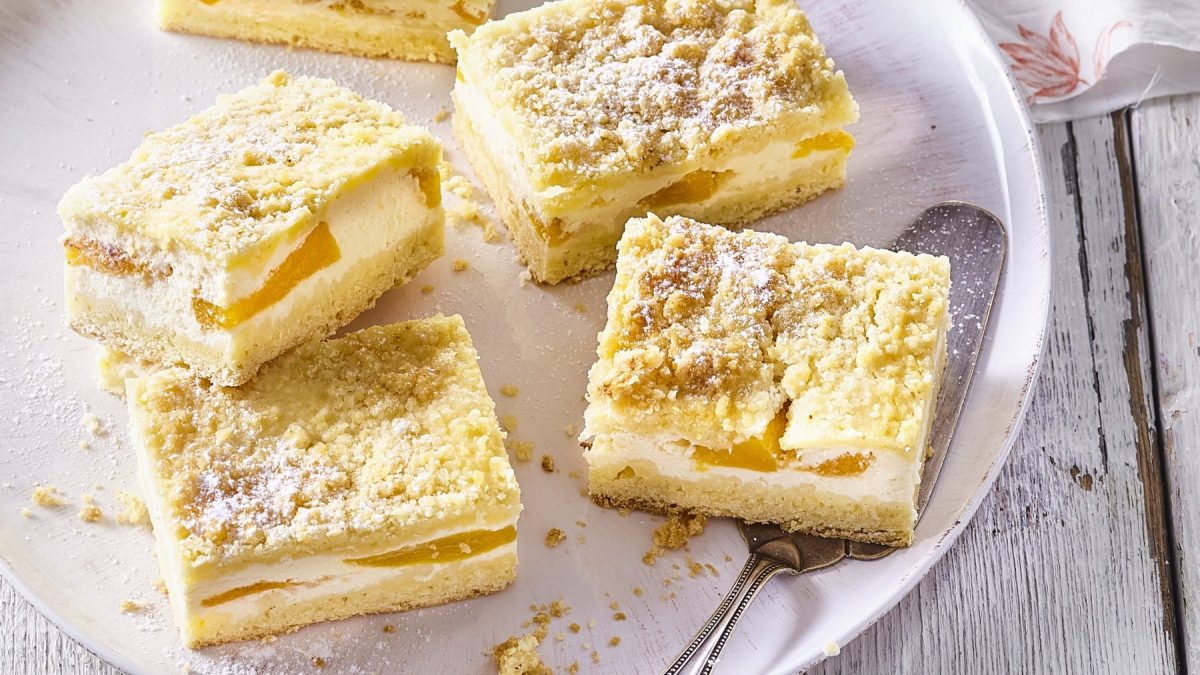 Ein weißes Tablett mit Vanillepudding-Schnitten mit Pfirsich auf einem weißen Holztisch.