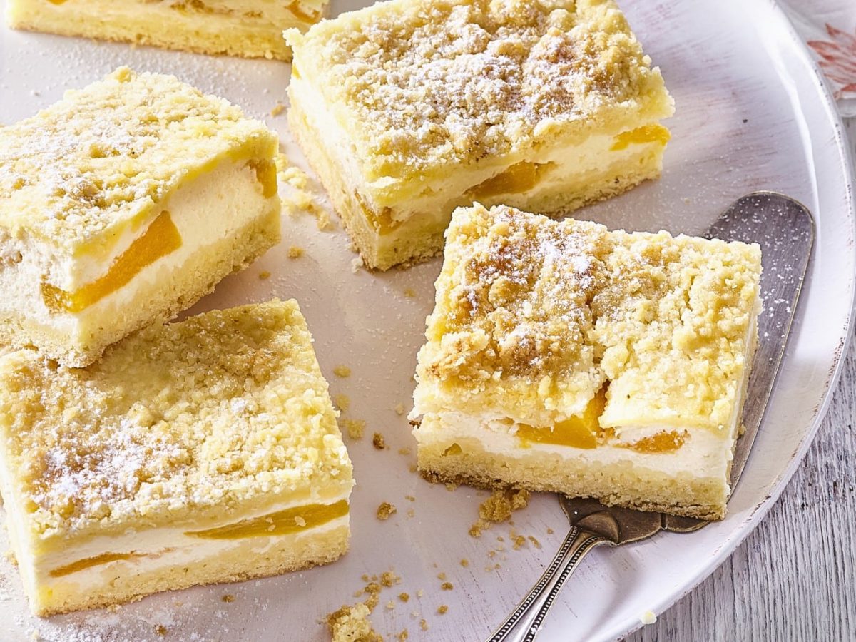 Ein weißes Tablett mit Vanillepudding-Schnitten mit Pfirsich auf einem weißen Holztisch.