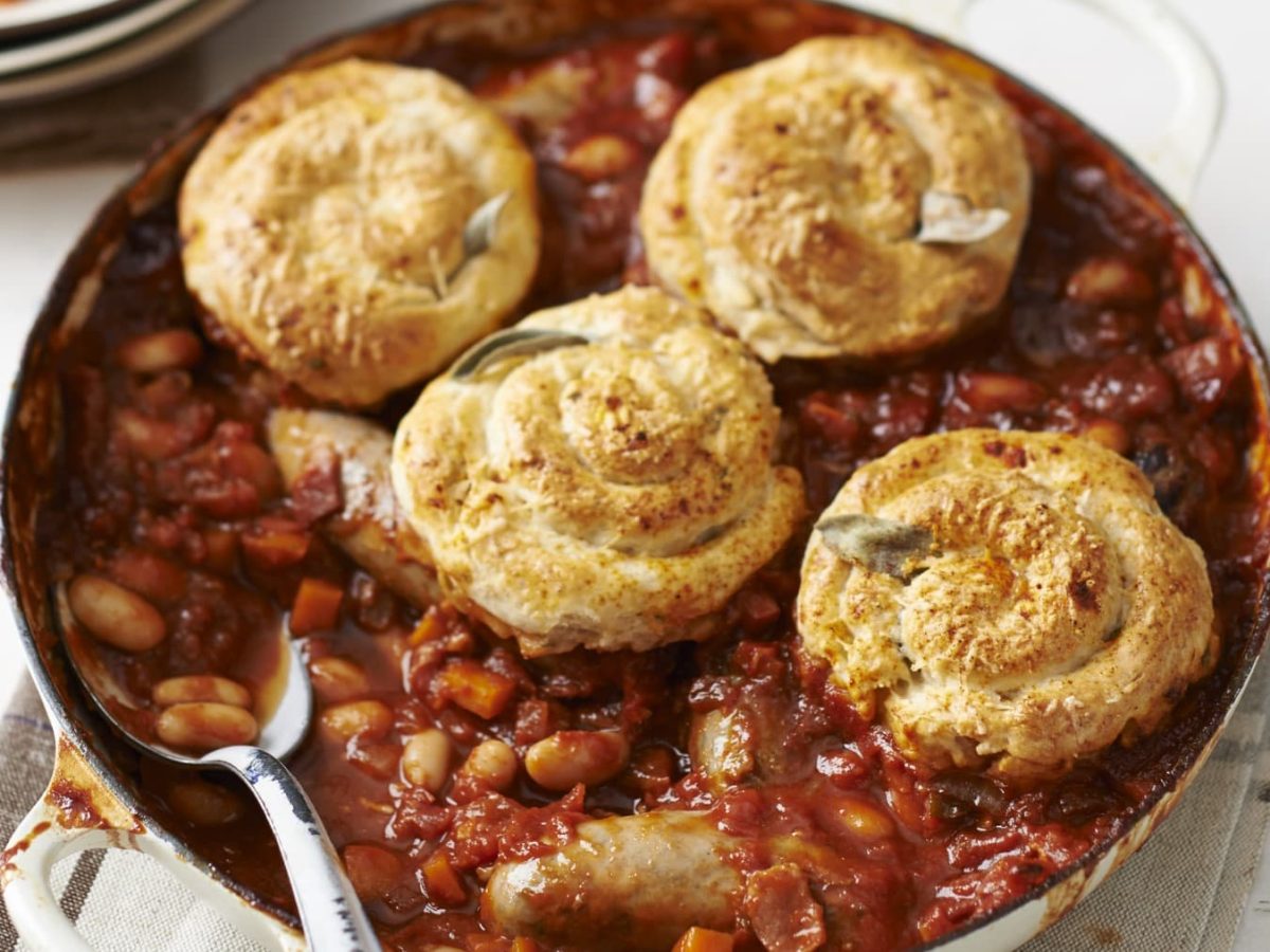 Wurst-Parmesan-Cobbler in einer Ofenform mit Löffel drin vor hellem Hintergrund.