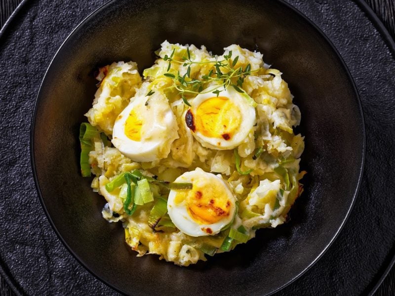 Anglesey Eggs – überbackene Eier auf Kartoffelpüree in Käsesauce auf schwarzem Teller.