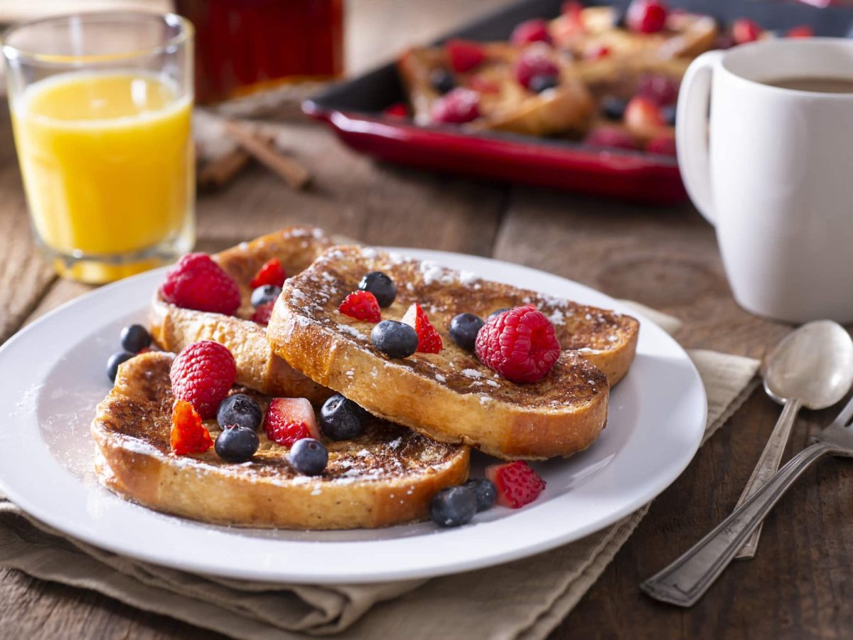 Arme Ritter mit Beeren und Puderzucker auf weißem Teller.