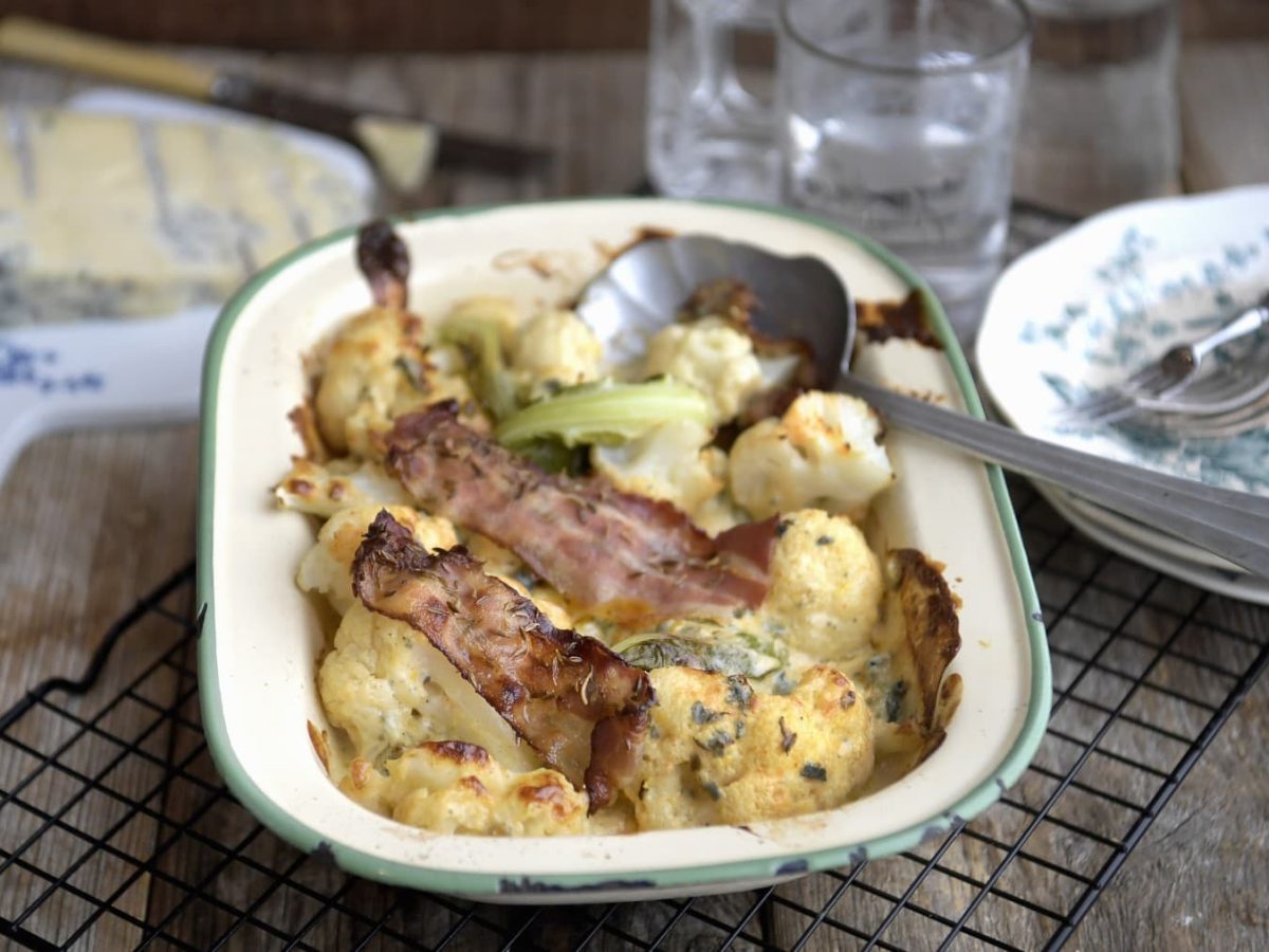 Blumenkohlgratin mit Blauschimmelkäse und geröstetem Speck, serviert in einer klassischen Auflaufform auf einem Gitter.