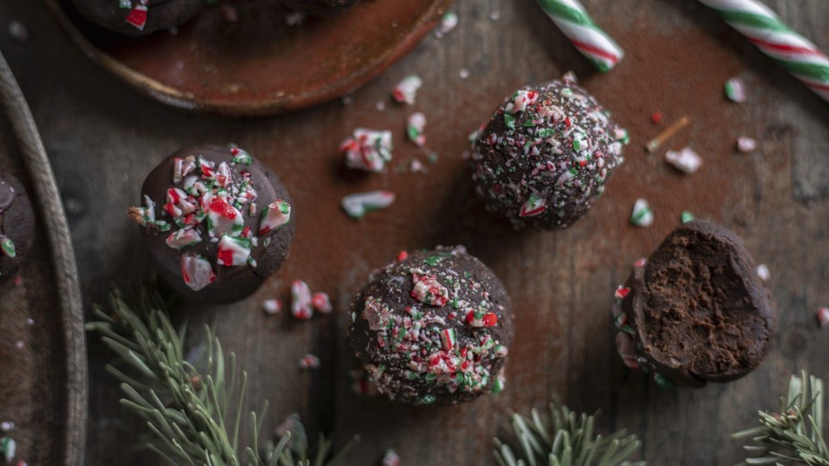 Vier Brownie-Minz-Trüffel garniert mit Zuckerstangen-Splittern vor Holzhintergrund.