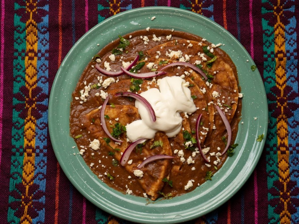 Enfrijoladas mexicanas in türkisem Teller auf bunter Decke. Draufsicht.