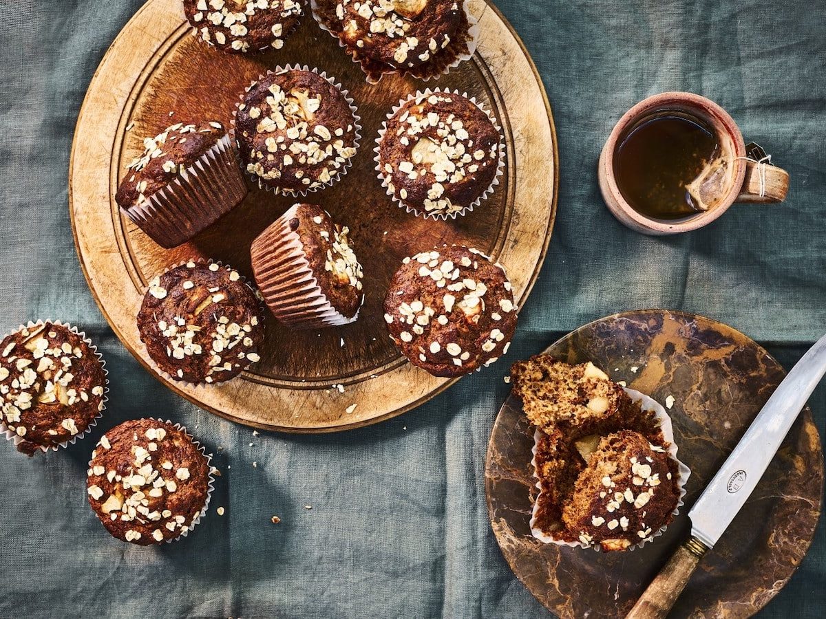 Apfelmuffins bestreut mit Haferflocken serviert auf einem braunen Holzteller und einer Tasse Tee