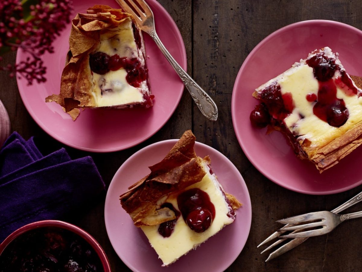 Auf einem Tisch stehen mehrere Teller mit Gewürz-Kirsch-Käsekuchen. Sie sind cremig und saftig.