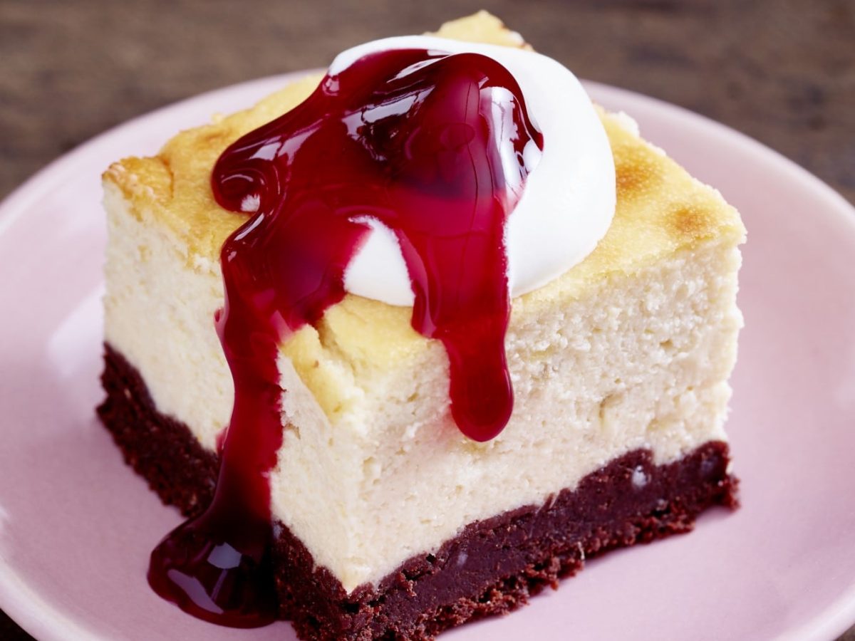 Ein Stück Käsekuchen mit Glühweinkirschen auf einem rosa Teller vor Holzhintergrund.