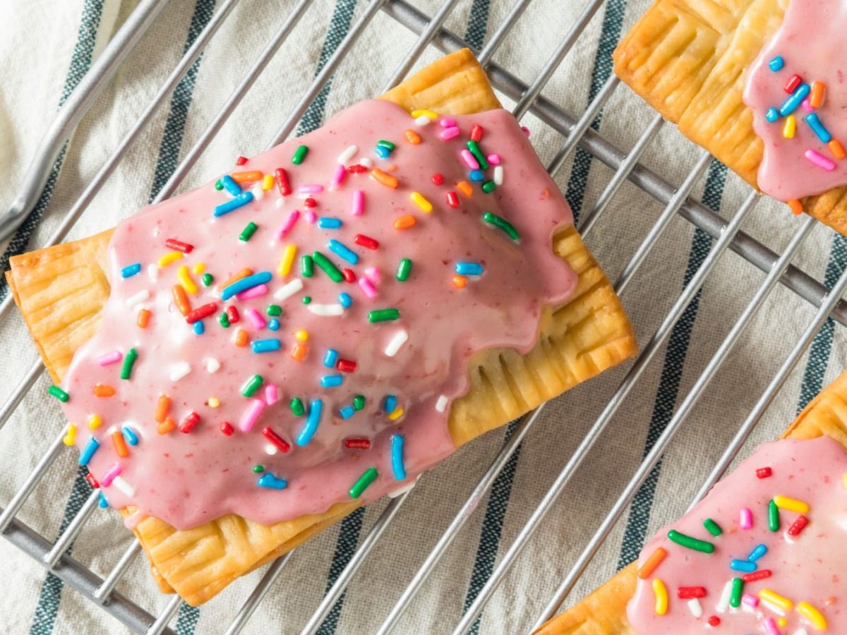 Selbst gemachte Pop Tarts mit rosa Guss und bunten Streuseln auf einem Gitter mit Küchentuch im Hintergrund.