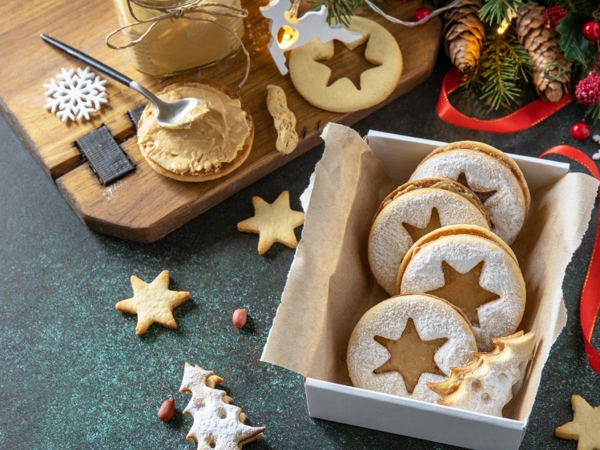 In einer Dose sind Linzer Plätzchen mit Erdnussbutter gelegt. Sie sind mit Puderzucker bestreut.