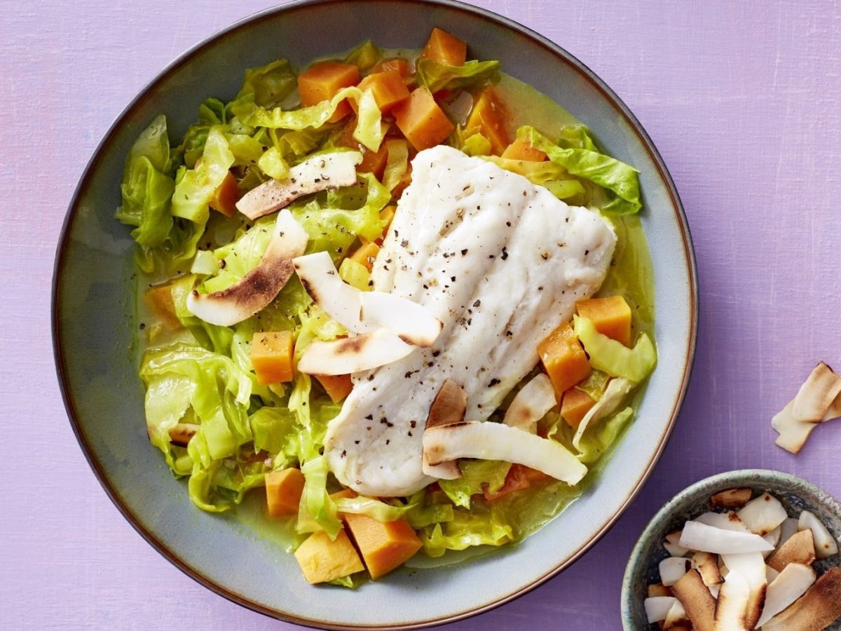 Süßkartoffelcurry mit Kabeljaufilet, Lauch und Kokosraspeln, serviert in einer Keramikschale, garniert mit frischem Pfeffer.