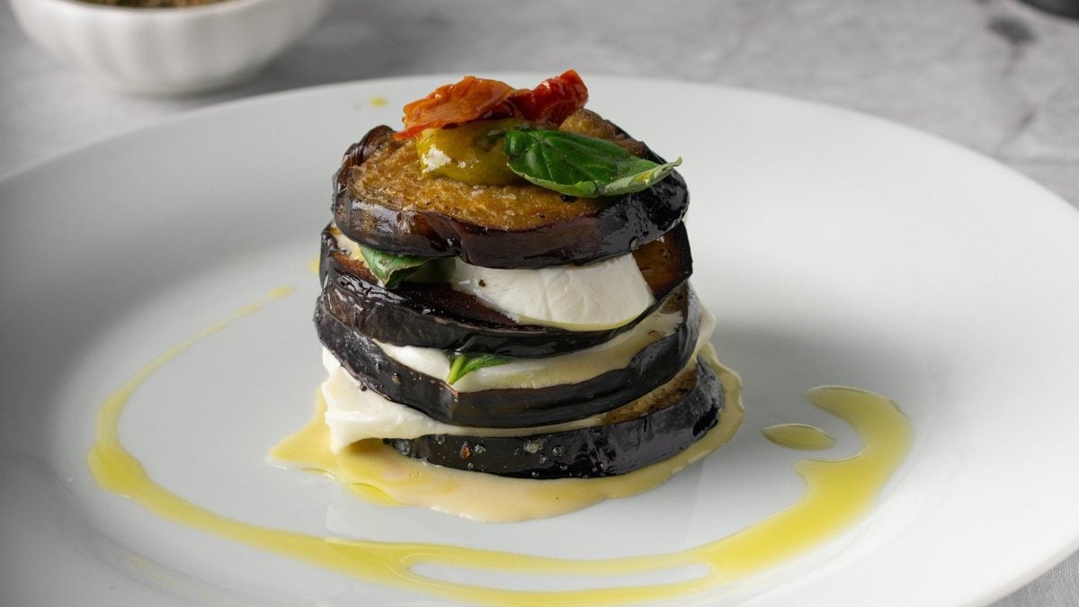 Ein Aubergine-Caprese-Türmchen mit Basilikum auf einem Teller mit Öl.