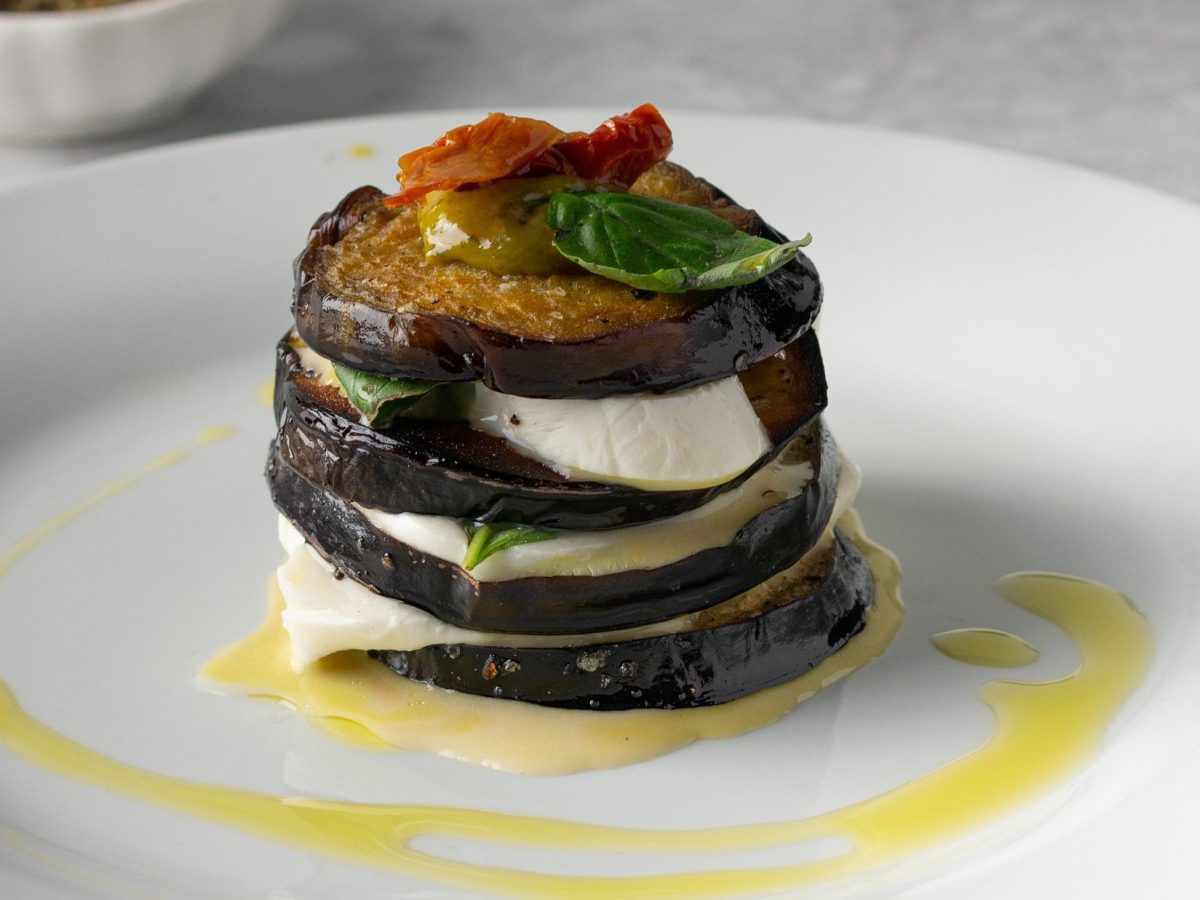 Ein Aubergine-Caprese-Türmchen mit Basilikum auf einem Teller mit Öl.