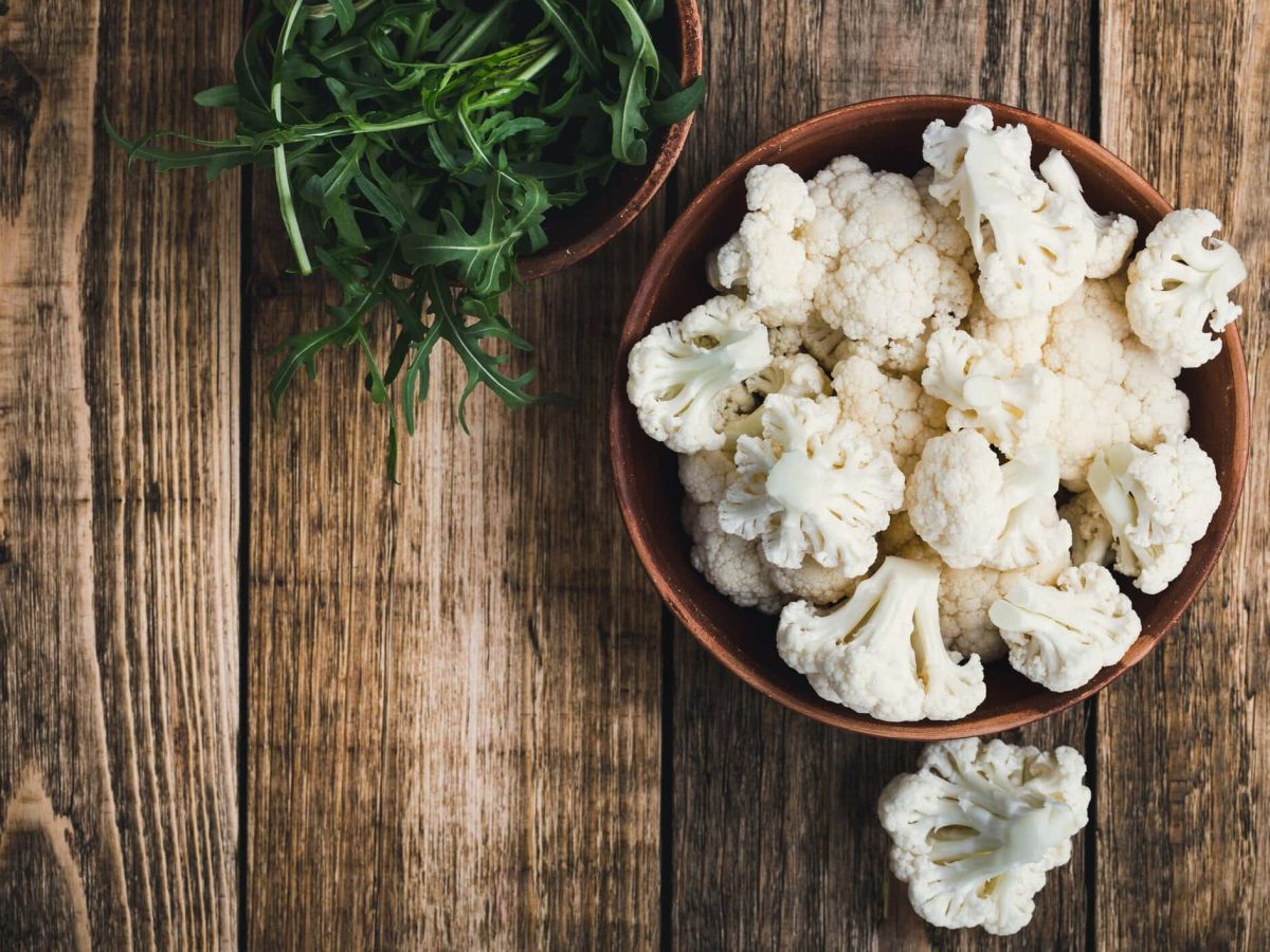 Kann man Blumenkohl roh essen? Blumenkohlröschen in einer Holzschale auf Holtisch. Daneben Salat. Draufsicht.