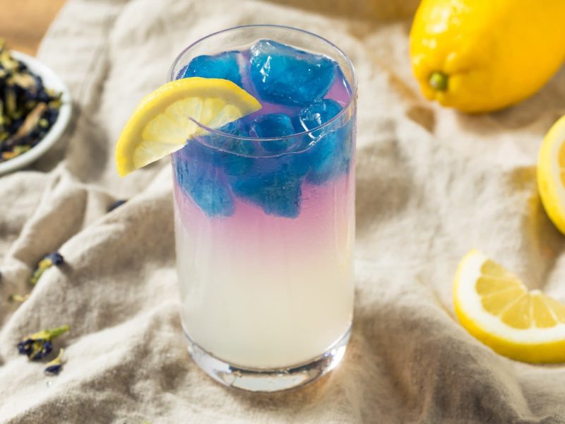 Ein Glas mit der gelben Zitronenmarmelade udn blauen Eiswürfeln.