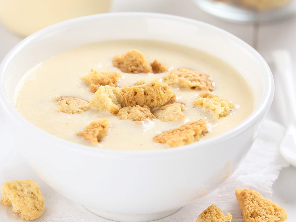 Eine weiße Schale mit der Buttermilch-Mousse auf einem weißen Tisch mit zerbrochenen Keksen.