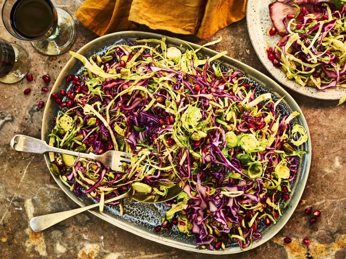 Coleslaw mit Pistazien, Granatapfelkernen und Orangen-Sauce, serviert auf einem flachen Servierteller auf einem steinernen Tisch.