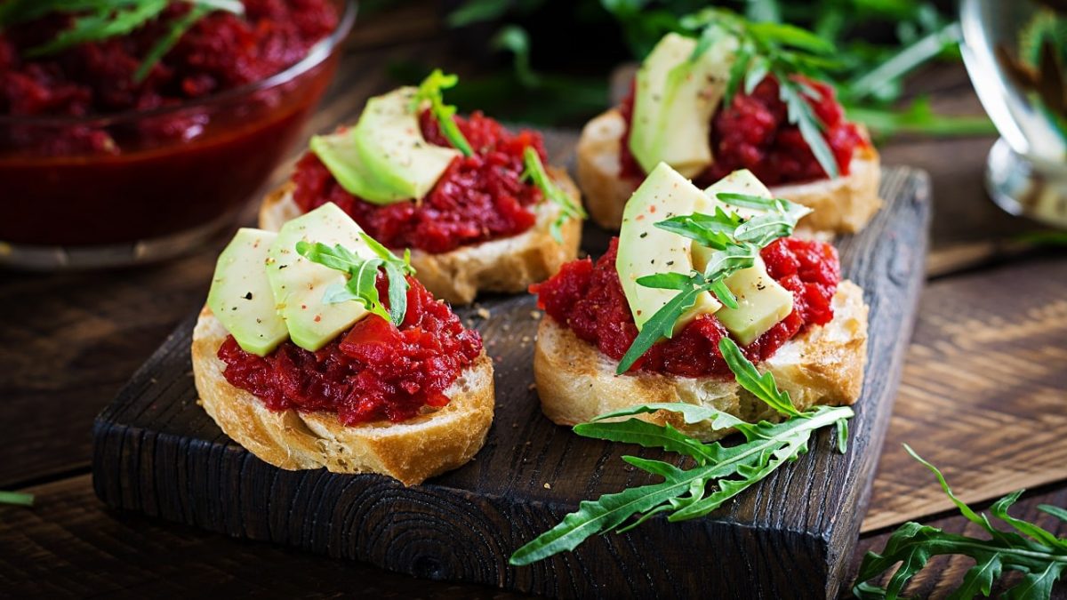 Draufsicht: Vier Crostini mit Rote-Bete-Relish und Apfel. liegen auf einem Holzbrett.