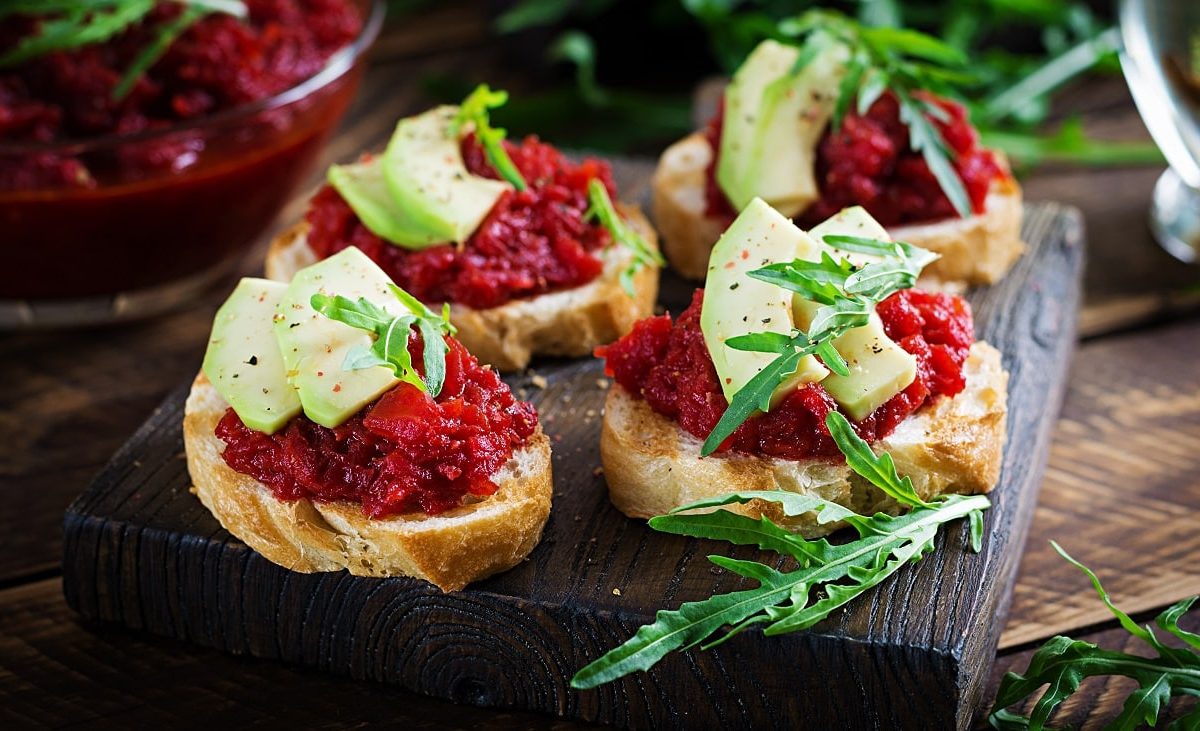 Draufsicht: Vier Crostini mit Rote-Bete-Relish und Apfel. liegen auf einem Holzbrett.