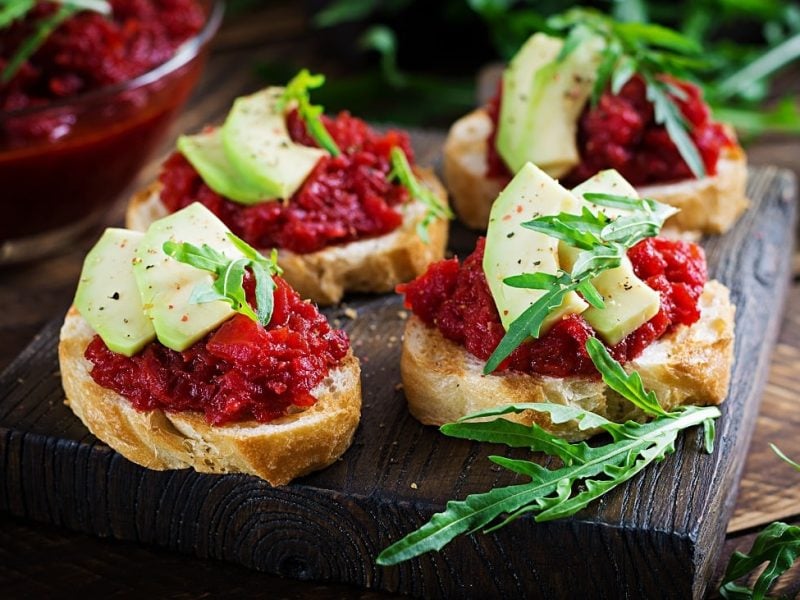 Draufsicht: Vier Crostini mit Rote-Bete-Relish und Apfel. liegen auf einem Holzbrett.