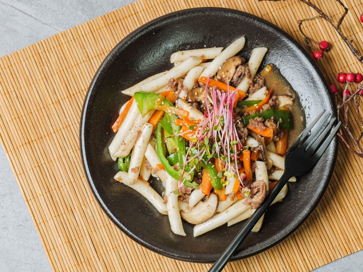 Ein schwarzer Teller mit Gungjung Tteokbokki auf einer Bambusmatte