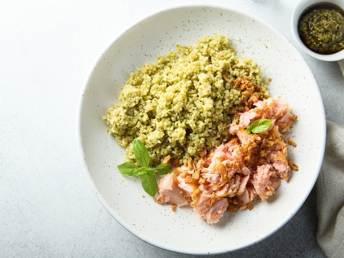 Ein weißer runder Teller mit Knusper-Lachs mit Pesto-Couscous.