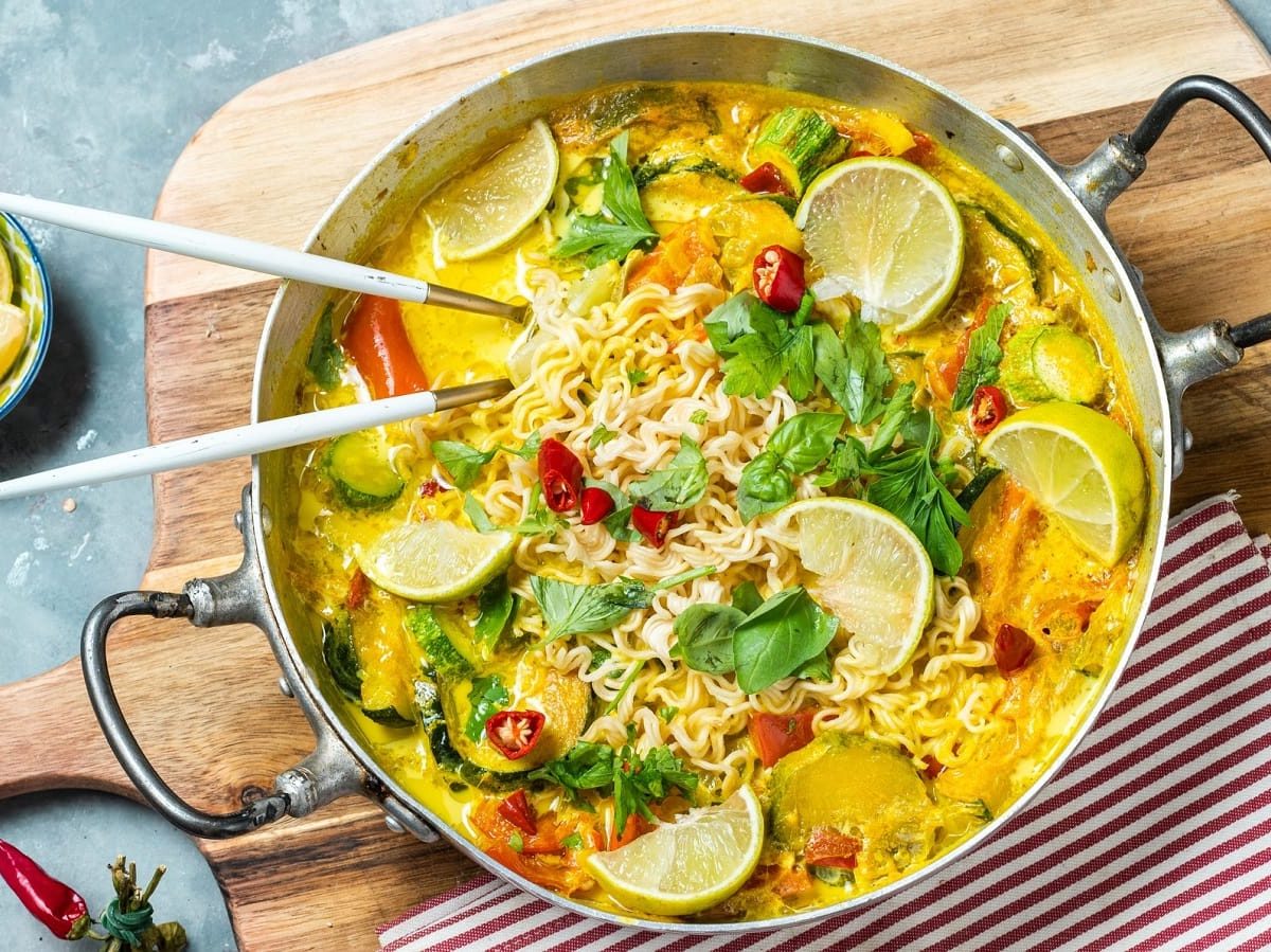 Eine große Schüssel mit Thai-Curry-Nudelsuppe auf einem Holzbrett.