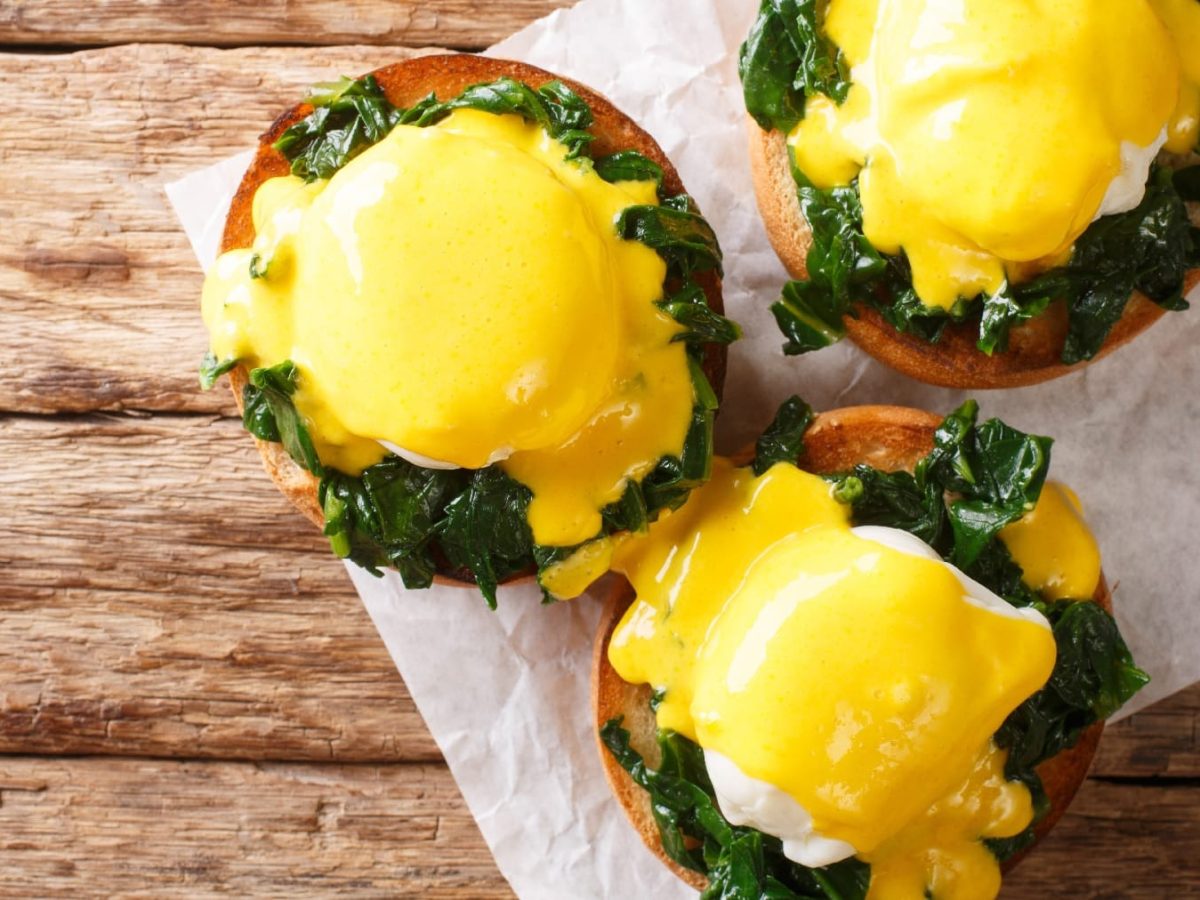 Drei Brötchen mit den Eggs Florentine auf Backpapier und einem dunklen Holztisch von oben fotografiert.