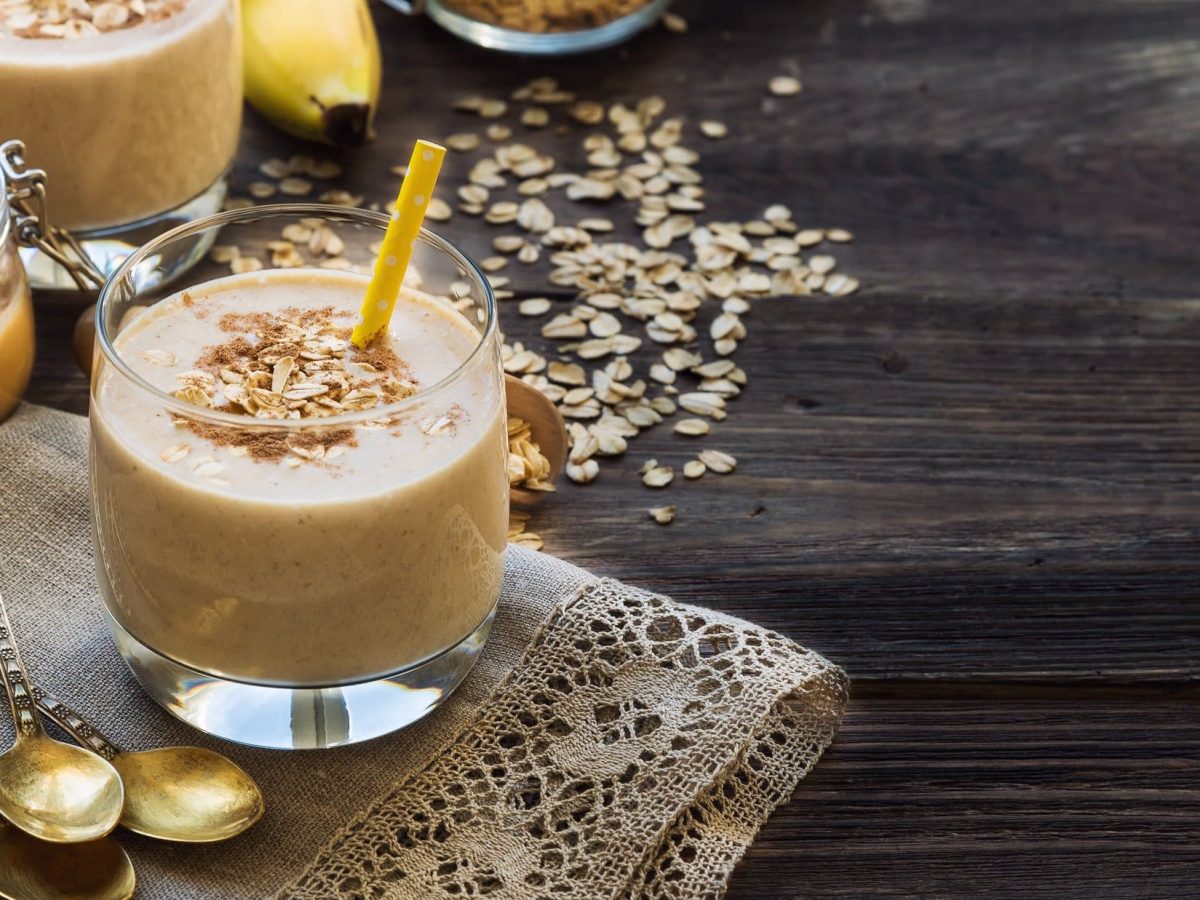 Zwei Gläser Erdnussbutter-Bananen-Smoothie mit Strohhalm und Haferflocken.