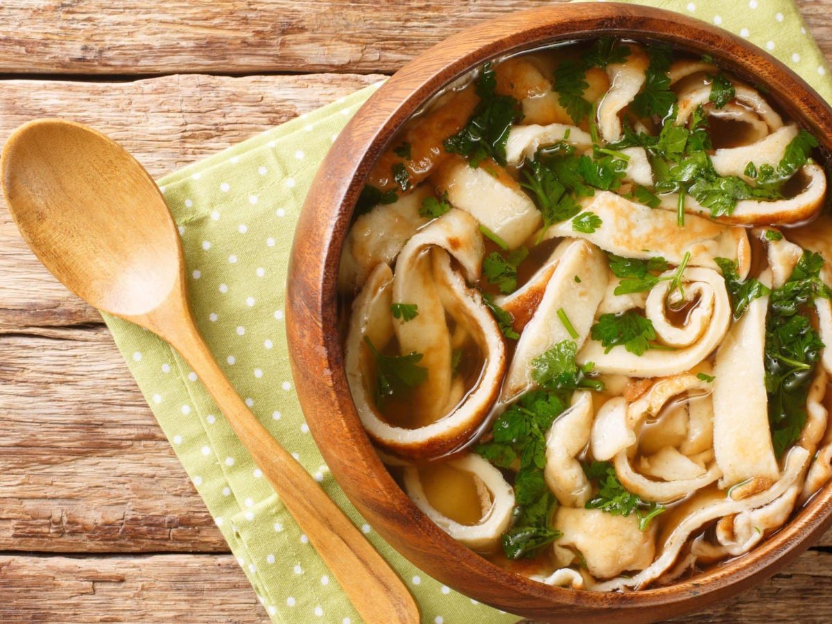 Eine warme braune Schüssel auf einem Holztisch mit der Frittatensuppe.