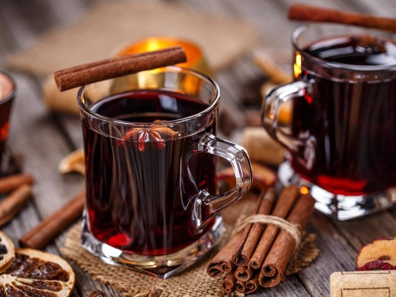 Zwei Gläser mit Glühwein mit Rum und Tee, drumherum liegen viele Gewürze wie Zimtstangen, Anis und getrocknetes Obst.