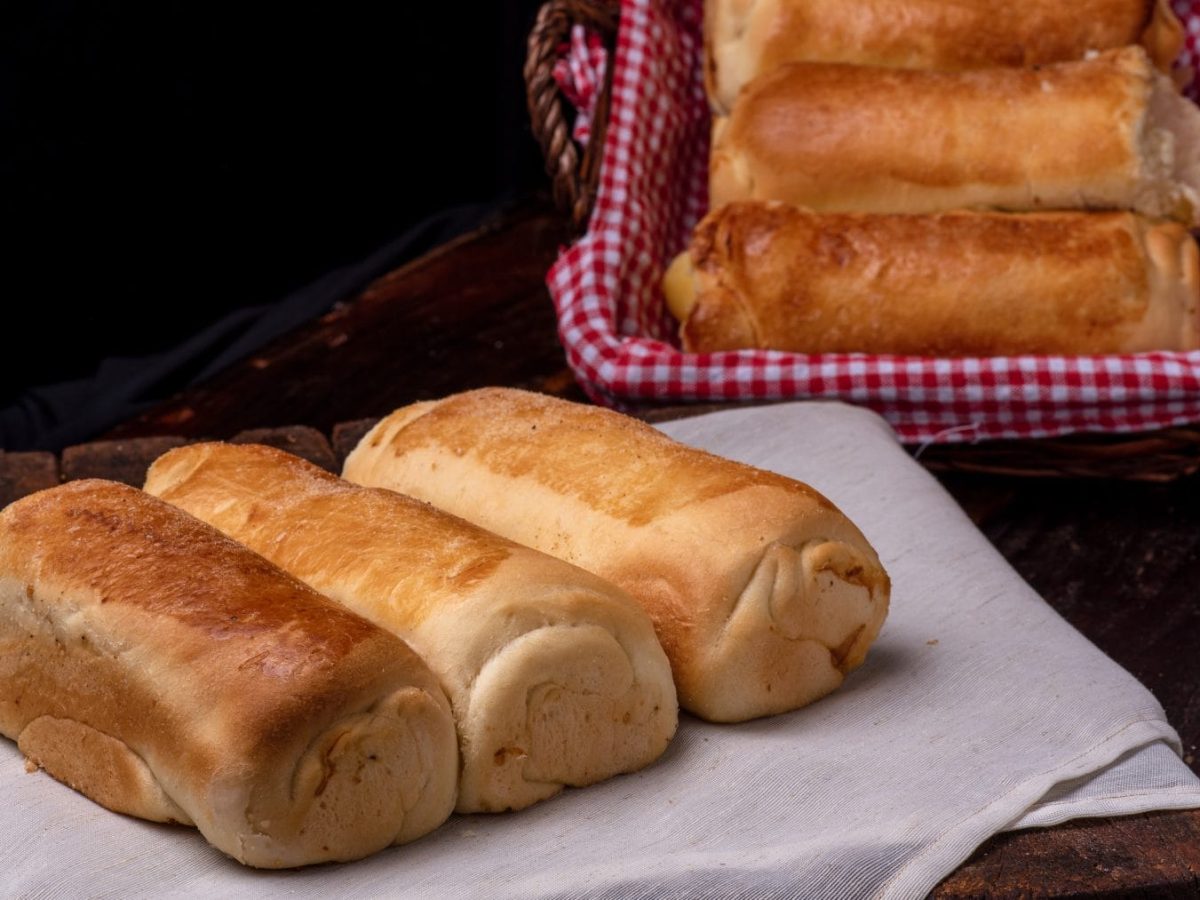 Original selbst gemachte Hoagie Rolls auf Holzbrett mit Stofftuch. Daneben Korb mit weiteren Hoagie Rolls. Draufsicht.